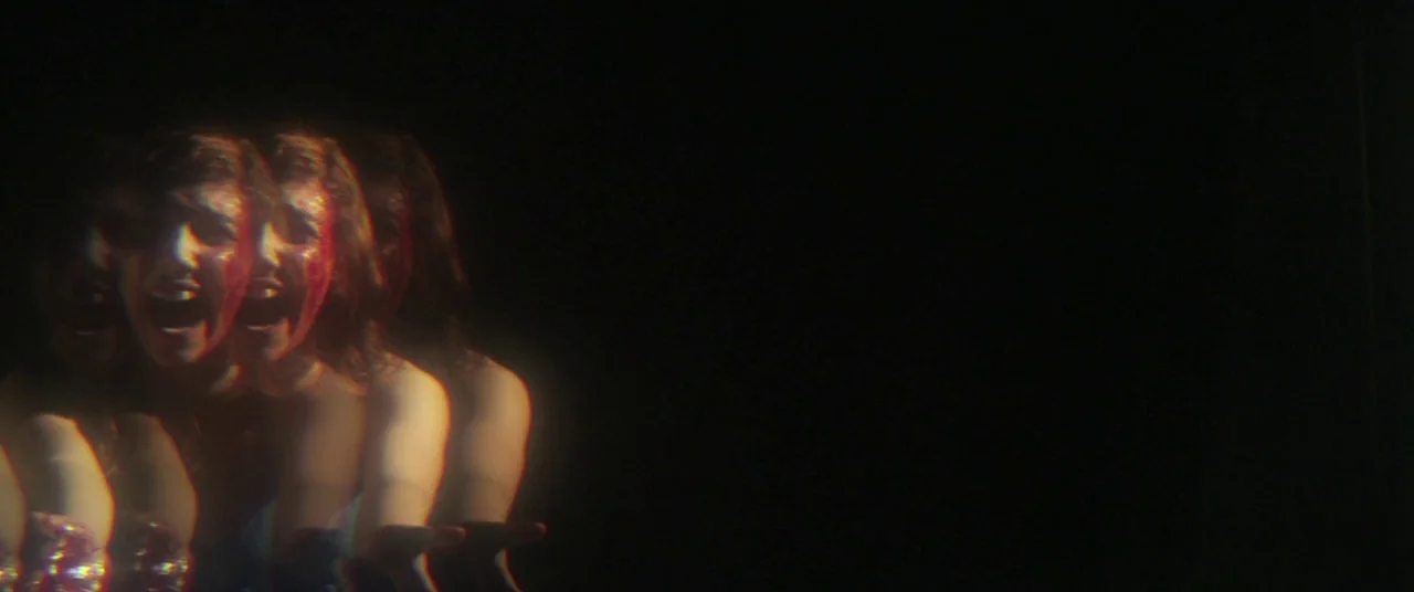 Here Comes The Devil (2012) movie still: closeup — A woman's face appears in a dark void against a solid black backdrop. She exhibits a…