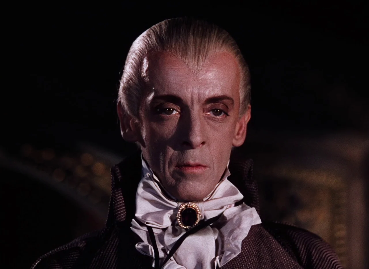 The Tales of Hoffmann (1951) movie still: closeup — The subject stands in a dimly lit, dark environment within an opulent interior space. The man…