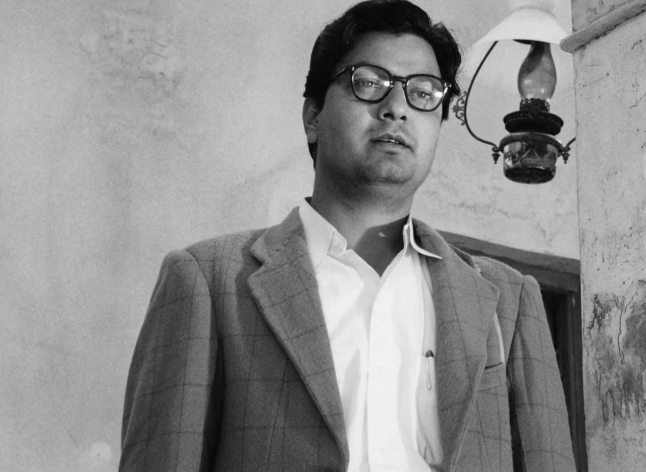 Apur Sansar (1959) movie still: medium — A stone portico with a mounted vintage wall lantern beside the subject. A man stands in the bright outdoor…