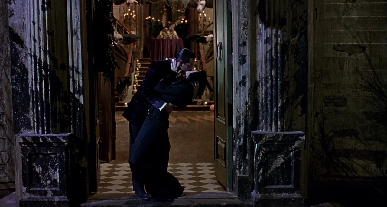 The Addams Family (1991) movie still: fullbody — An arched doorway framed by weathered wooden pillars leads into a dimly lit, candlelit hall. A…