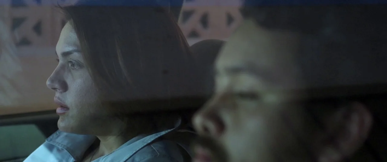 Here Comes The Devil (2012) movie still: medium — The interior of a car at night seen from the passenger window perspective. A woman sits in the…