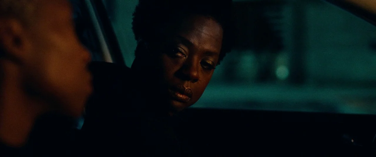 Widows (2018) movie still: medium — Inside a dark vehicle at night, the interior is lit by faint ambient light. A woman turns her head to look at a…