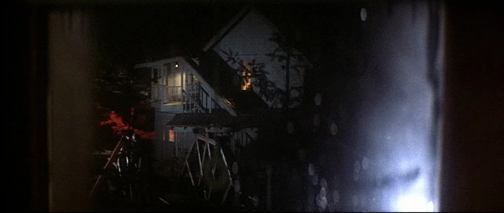 McCabe & Mrs.Miller (1971) movie still: establishing — A dark, two-story house stands at night seen through a window frame. A playground swing set…