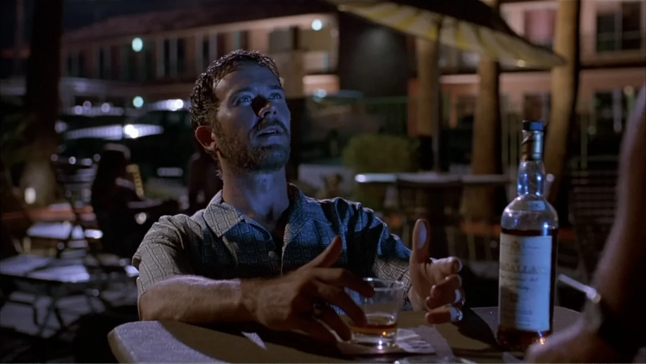 Ajuste de Cuentas (2016) movie still: medium — A dark outdoor hotel patio at night with a distant motel building visible behind. A man with short…
