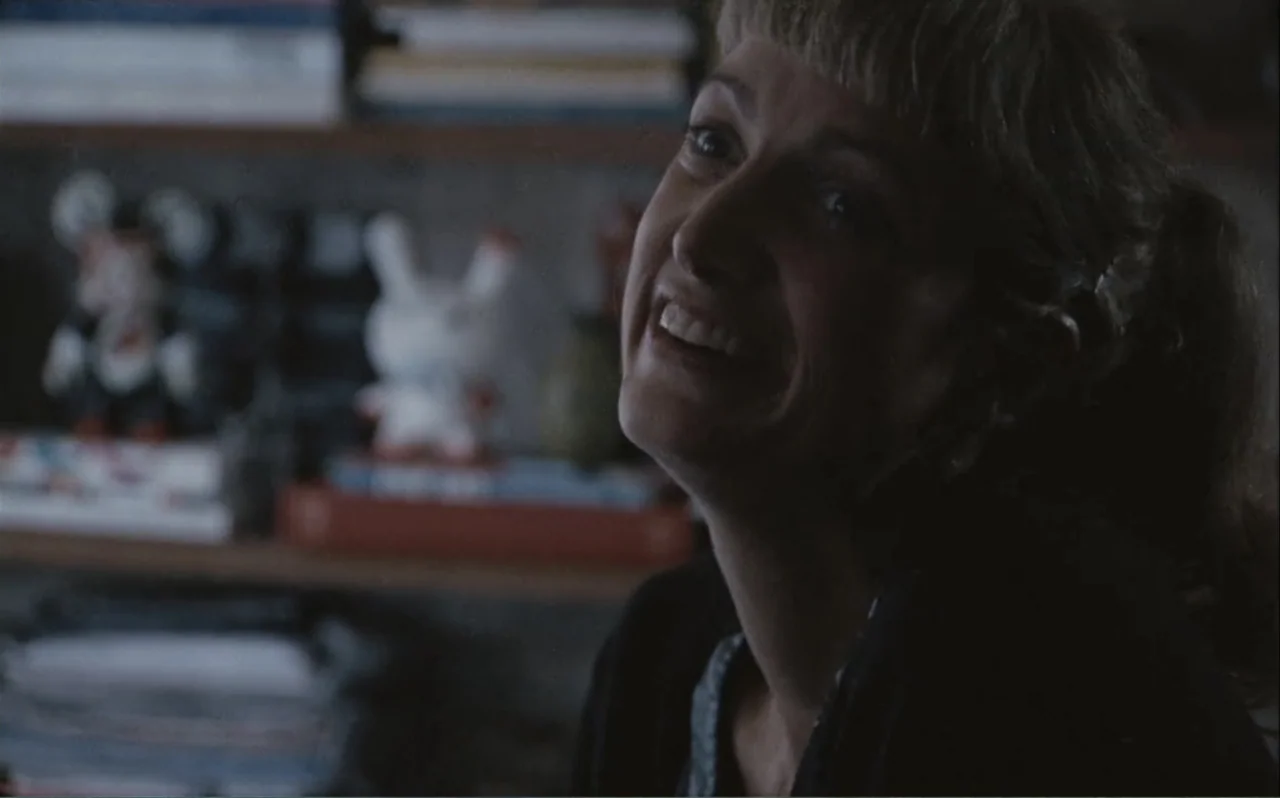 The Greasy Hands Preachers (2014) movie still: closeup — An indoor room with a cluttered shelf featuring small figures in the background. A woman in…