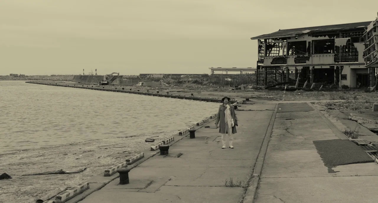 The Whispering Star (2015) movie still: wide — An abandoned seaside area features a dilapidated building with exposed framing and rubble nearby. A…