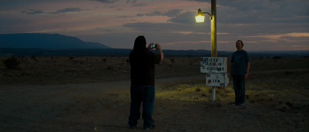 Paul (2011) movie still: wide — An arid desert landscape at twilight features distant mountains under a cloudy dusk sky. A man takes a picture of…