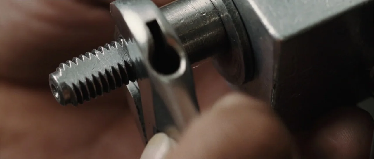 Inside Man (2006) movie still: closeup — A close-up view shows a metal wrench tightening a threaded bolt into a block. The mechanical components…