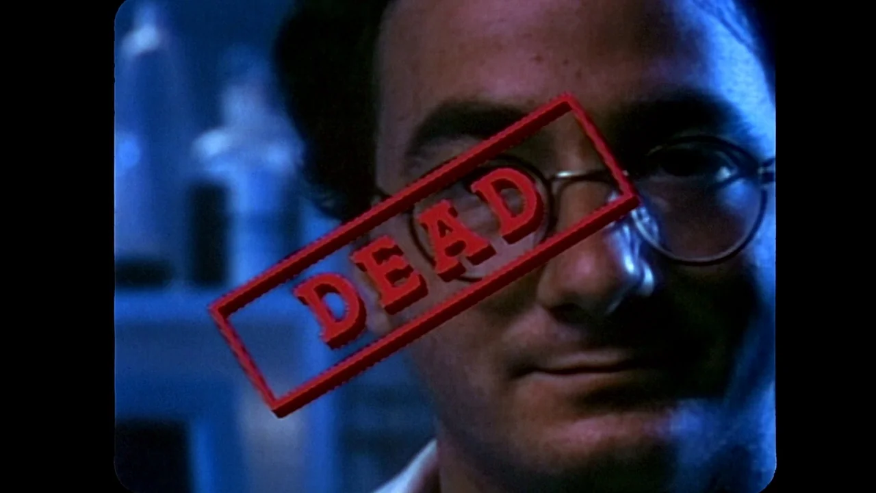 Jason Goes To Hell (1993) movie still: closeup — A dark, blue-lit room contains a blurred man wearing wire-rimmed spectacles. A red rectangular…