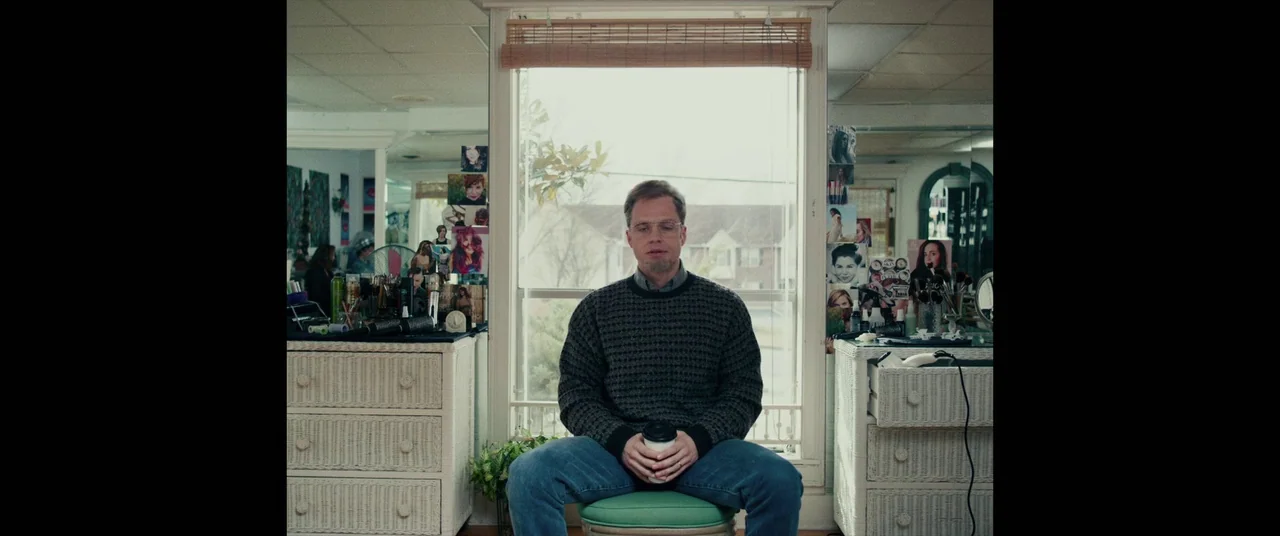 I, Tonya (2017) movie still: medium — A quiet salon interior features wicker cabinets and hair styling tools on both sides. A man sits on a stool…