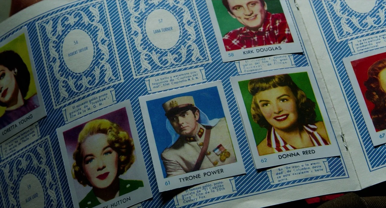 Pain and Glory (2019) movie still: closeup — A close-up view of a vintage sticker album page displaying multiple rectangular collector portraits.…