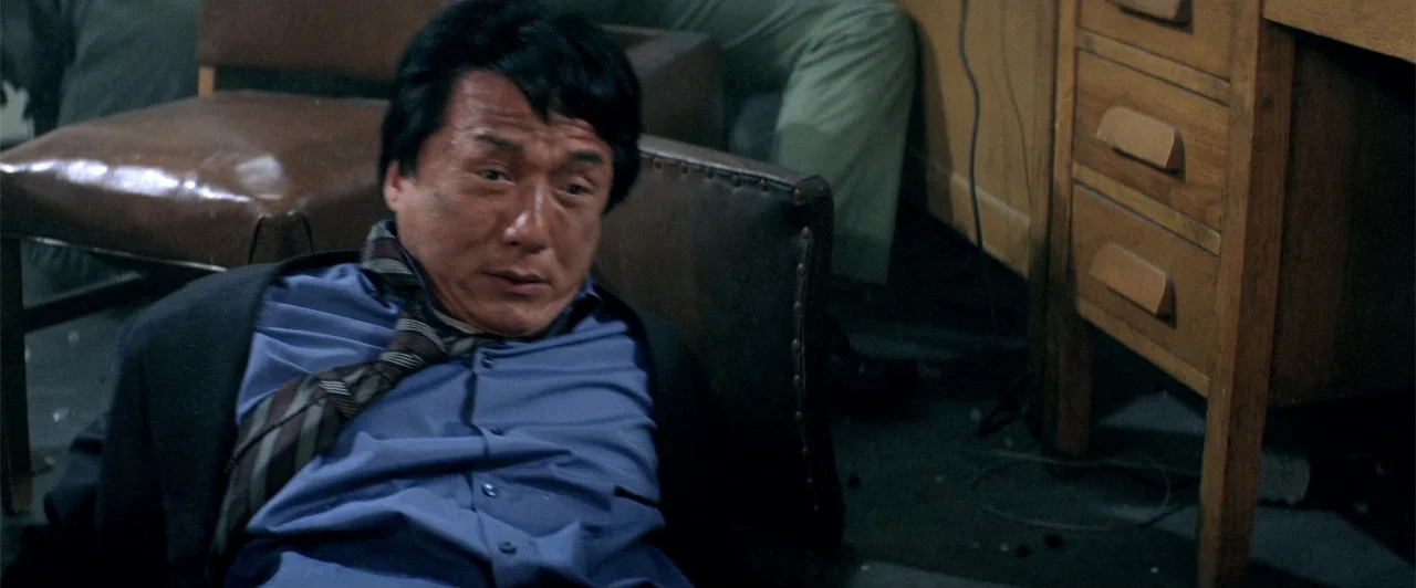 Rush Hour 2 (2001) movie still: medium — A dimly lit office features wooden furniture and an occupant sitting in a chair. A man in a blue dress…