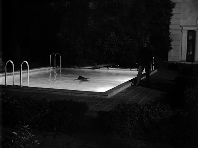 Sunset Boulevard (1950) movie still: wide — A lit backyard pool at night is surrounded by dense dark hedges and vegetation. A man in a dark suit…