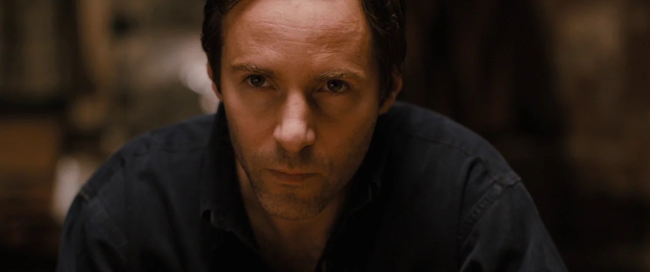 Ginger & Rosa (2012) movie still: closeup — A dark indoor space with indistinct textures visible in the blurred background. A man faces the camera…
