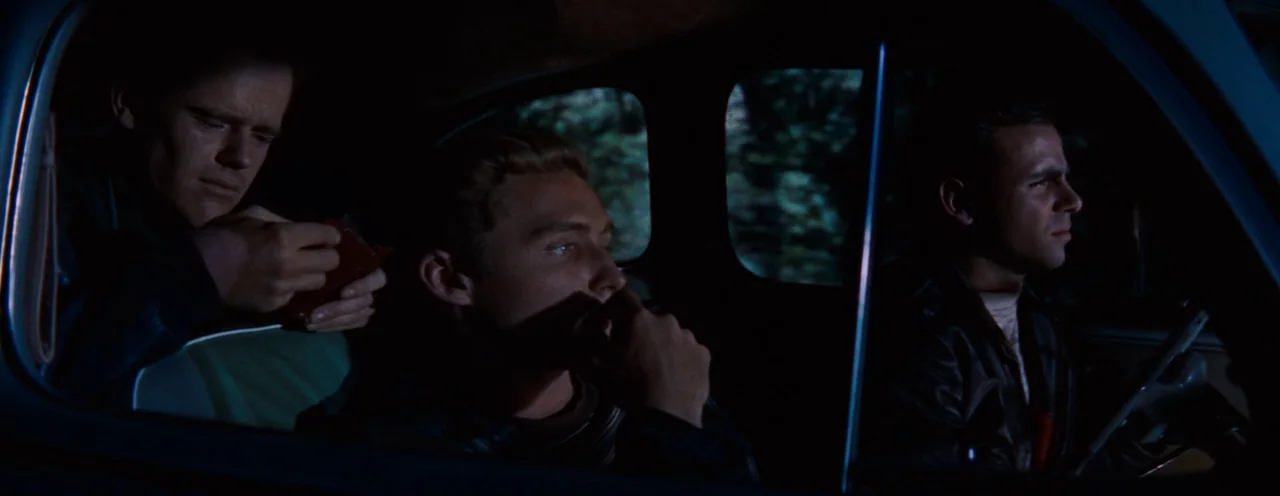 Rebel Without A Cause (1955) movie still: medium — Three young men sit inside a vehicle moving through a dark, wooded landscape at night. The driver…