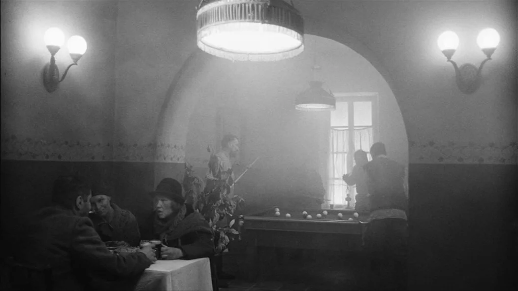 The Role (2013) movie still: wide — A dark, smoky tavern interior features a billiards table under a single overhead light. People sit at a nearby…