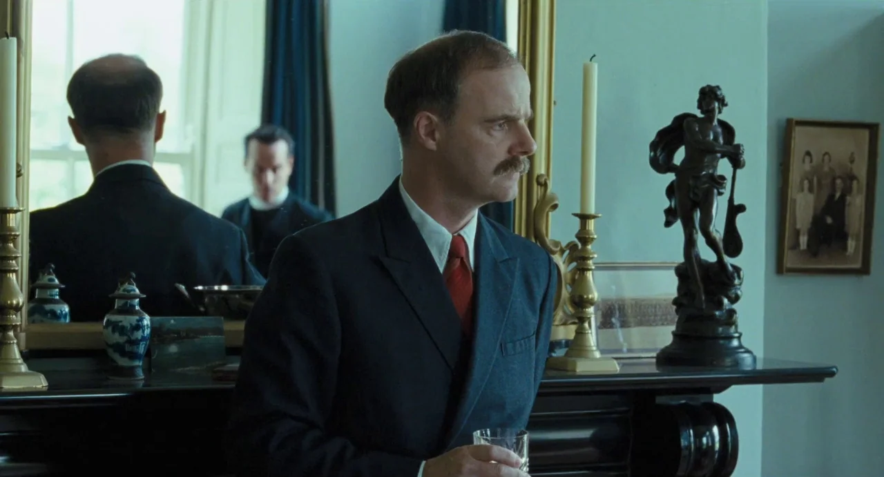 Jimmy’s Hall (2014) movie still: medium — A formal interior features a black mantle with a large mirror and bronze statue. A man in a suit stands…