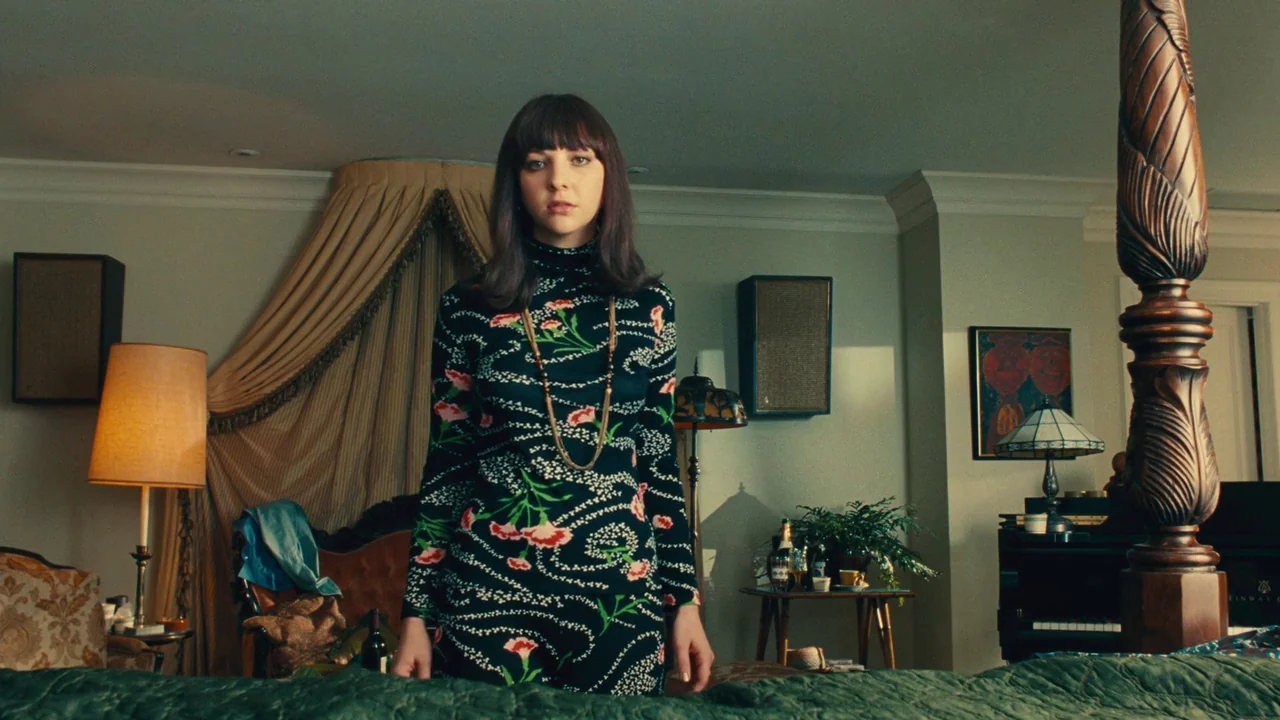 Love & Mercy (2014) movie still: medium — A hotel suite features 1970s decor including a canopy bed and dark wood furniture. A young woman in a…