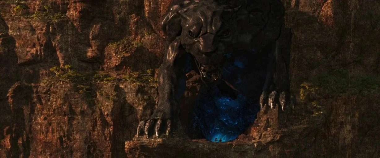 Black Panther (2018) movie still: wide — A colossal panther-shaped stone monument is carved directly into a steep brown rock canyon. Bright blue…