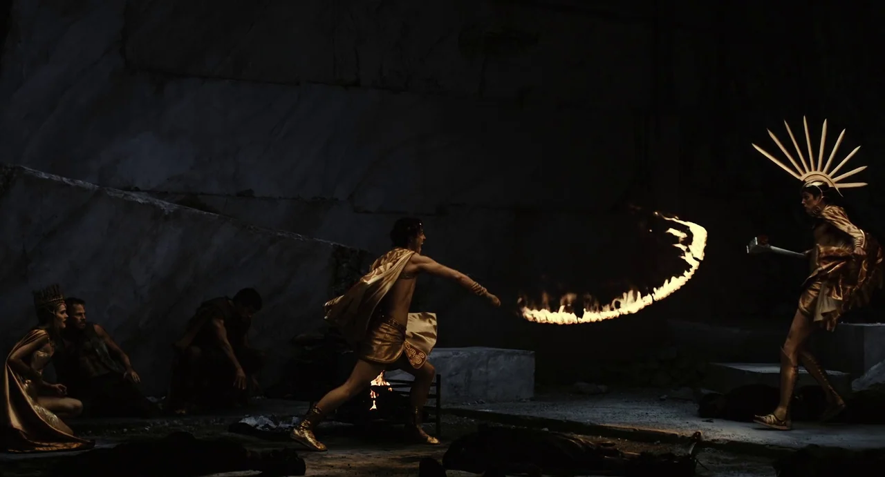 The Immortals (2011) movie still: wide — A dark, cavernous stone quarry with large jagged rock walls forming the backdrop. A warrior swings a whip…