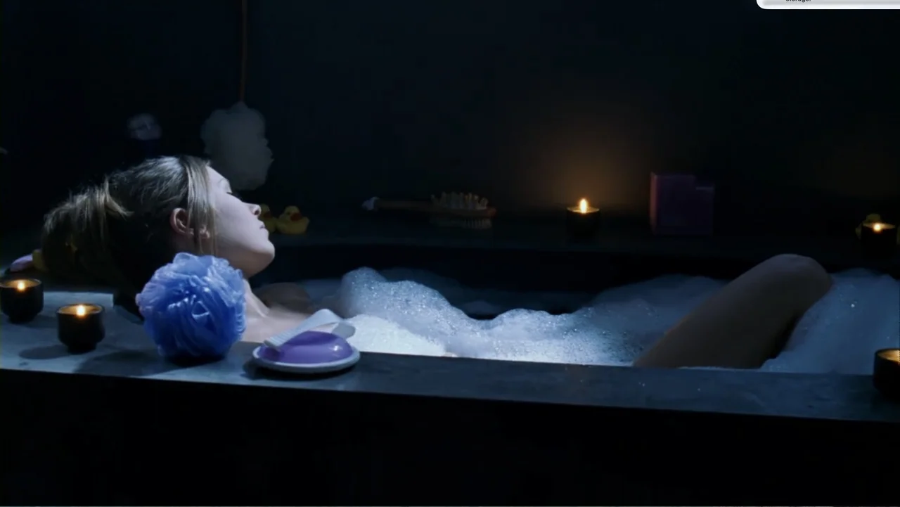 Chain Letter (2010) movie still: medium — A dark bathroom contains a bathtub filled with water and white soap bubbles. A woman rests her head back…