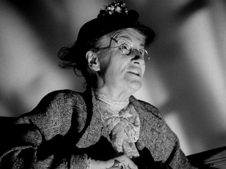 Stranger on the Third Floor (1940) movie still: closeup — An elderly woman sits in a dark space against a patterned, light-colored background. She…