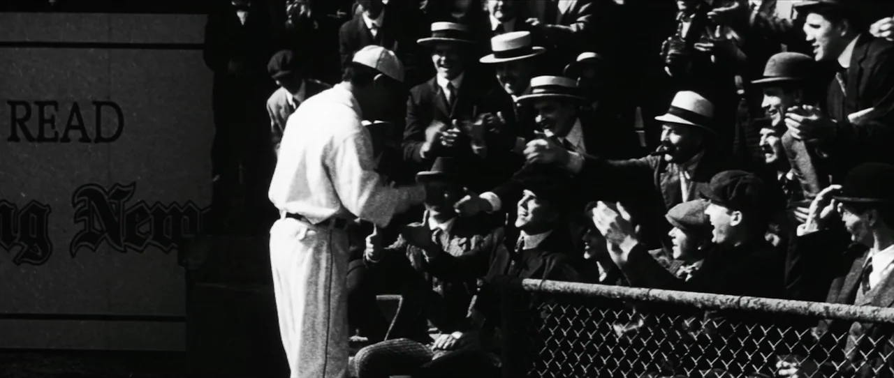 Cobb (1994) movie still: medium — A 1920s baseball stadium stands with spectators packed into wooden bleachers near a chain-link fence. A baseball…