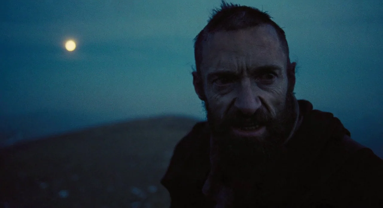 Les Misérables (2012) movie still: closeup — A man stands on a dark, desolate hillside under the light of a pale moon. He looks off-camera with a…