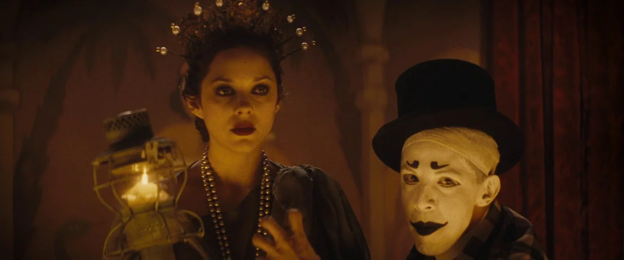 The Immigrant (2013) movie still: medium — A dimly lit tent interior features patterned walls obscured by deep golden shadow. A woman in a crown…