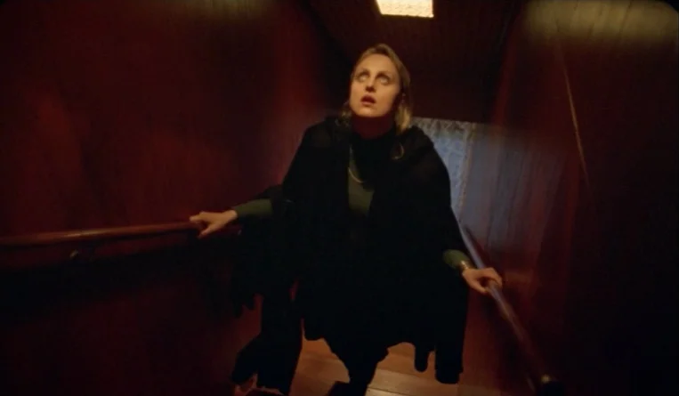 The Turn of the Century (2001) movie still: medium — A narrow staircase is enclosed by dark wood-paneled walls on both sides. A woman wearing a…