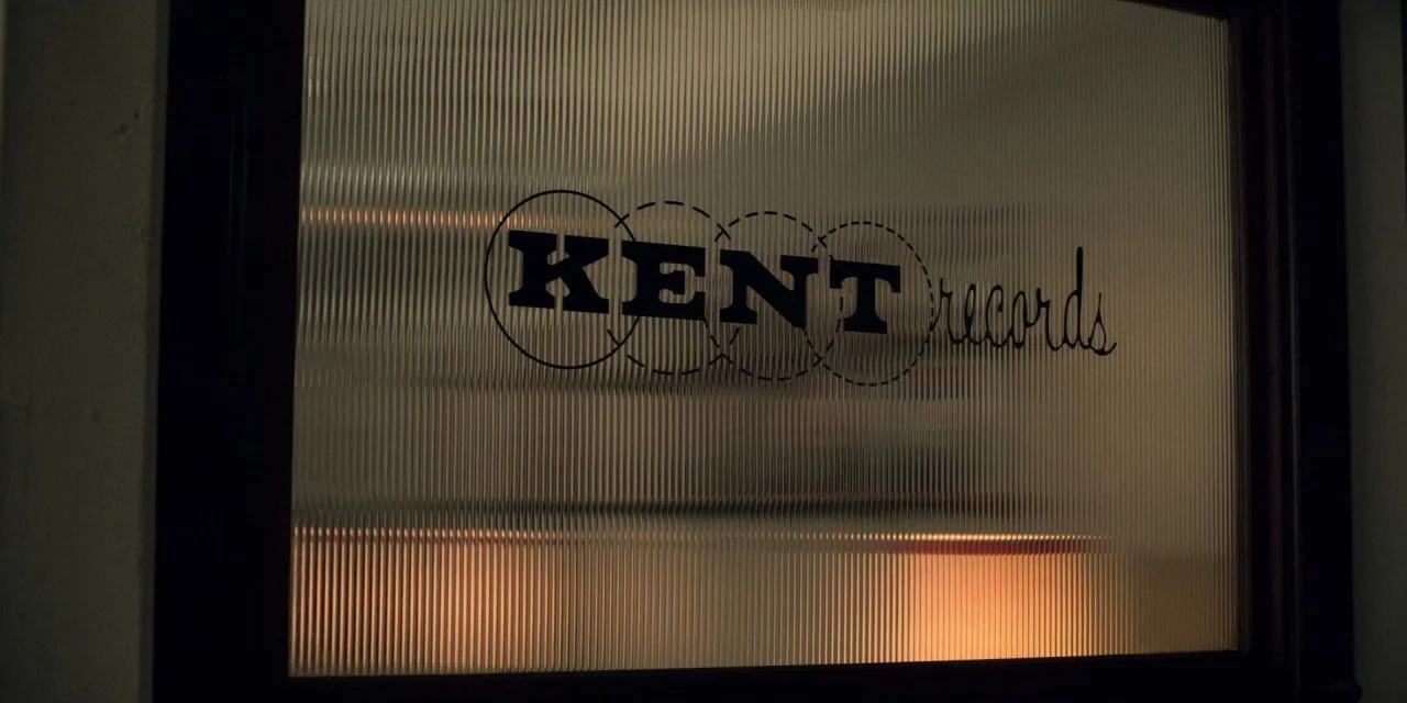 Dolemite Is My Name movie still: closeup — A close view of a fluted glass office door panel features black lettering. The text reads Kent Records…