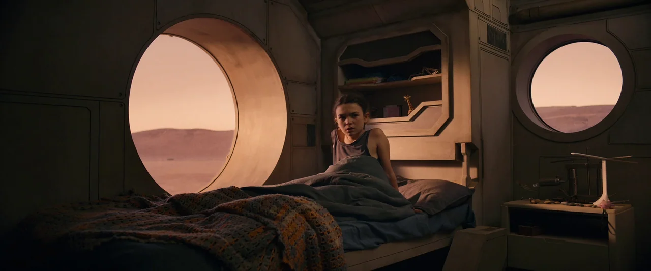 Settlers (2021) movie still: medium — A futuristic quarters with rounded observation windows looking out onto a barren orange planet. A young girl…