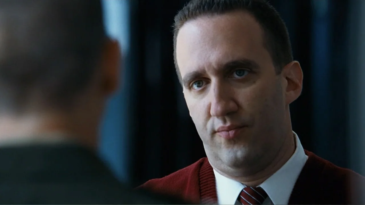 Taking Chances (2011) movie still: closeup — A modern office interior featuring dark walls and minimalist professional decor. A man in a burgundy…