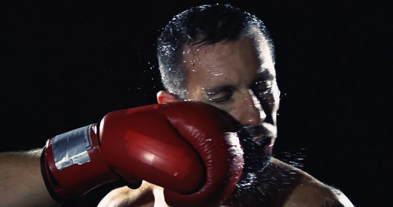 Violet (2021) (2021) movie still: closeup — A dark, void-like space emphasizes the impact of a physical confrontation. A boxer receives a forceful…