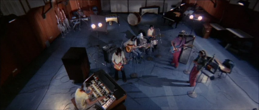 Four Flies On Grey Velvet (1971) movie still: wide — A spacious, dim recording studio features wooden walls and various musical instruments on the…