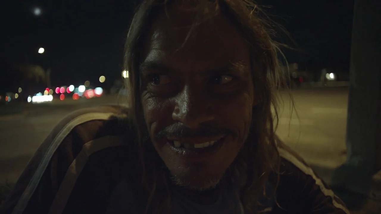Florida Man (2015) movie still: closeup — An outdoor urban environment at night with distant bokeh lights in the background. A middle-aged man looks…