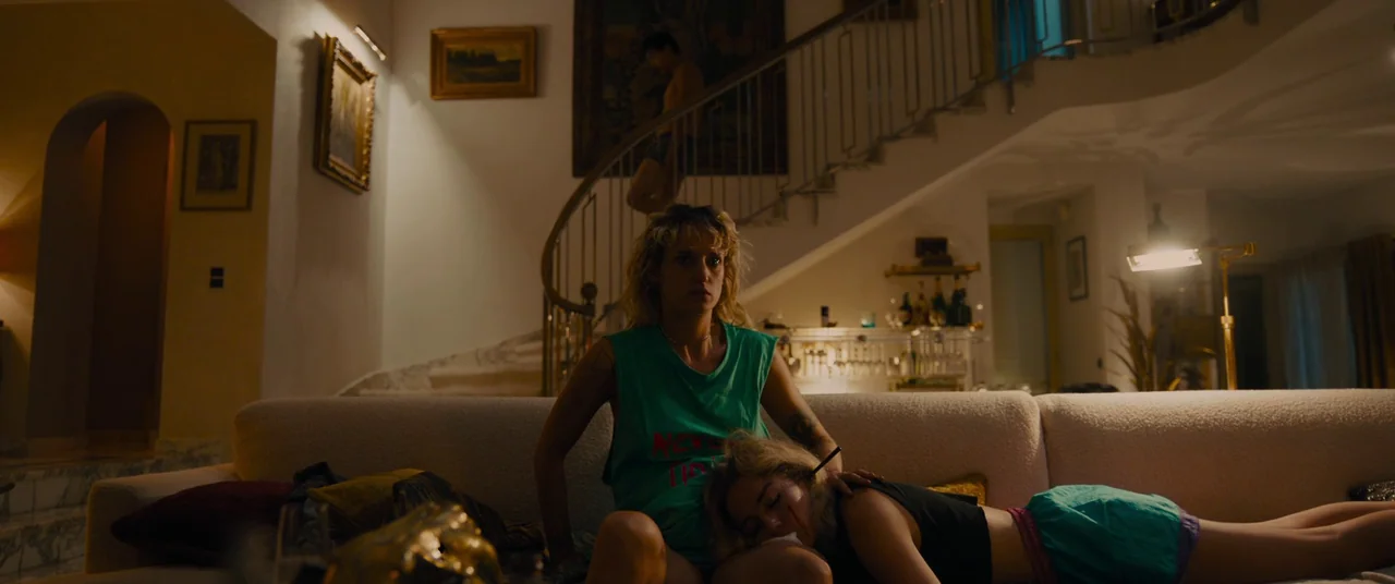 Titane (2021) movie still: medium — A spacious, modern multi-level foyer features a large winding staircase and high ceilings. Two young women…
