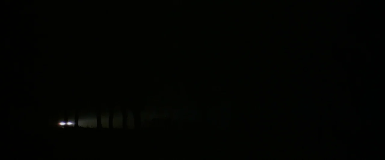 The Monster (2016) movie still: wide — A dark, expansive landscape at night features only a sliver of visible horizon line. Two distant, bright…