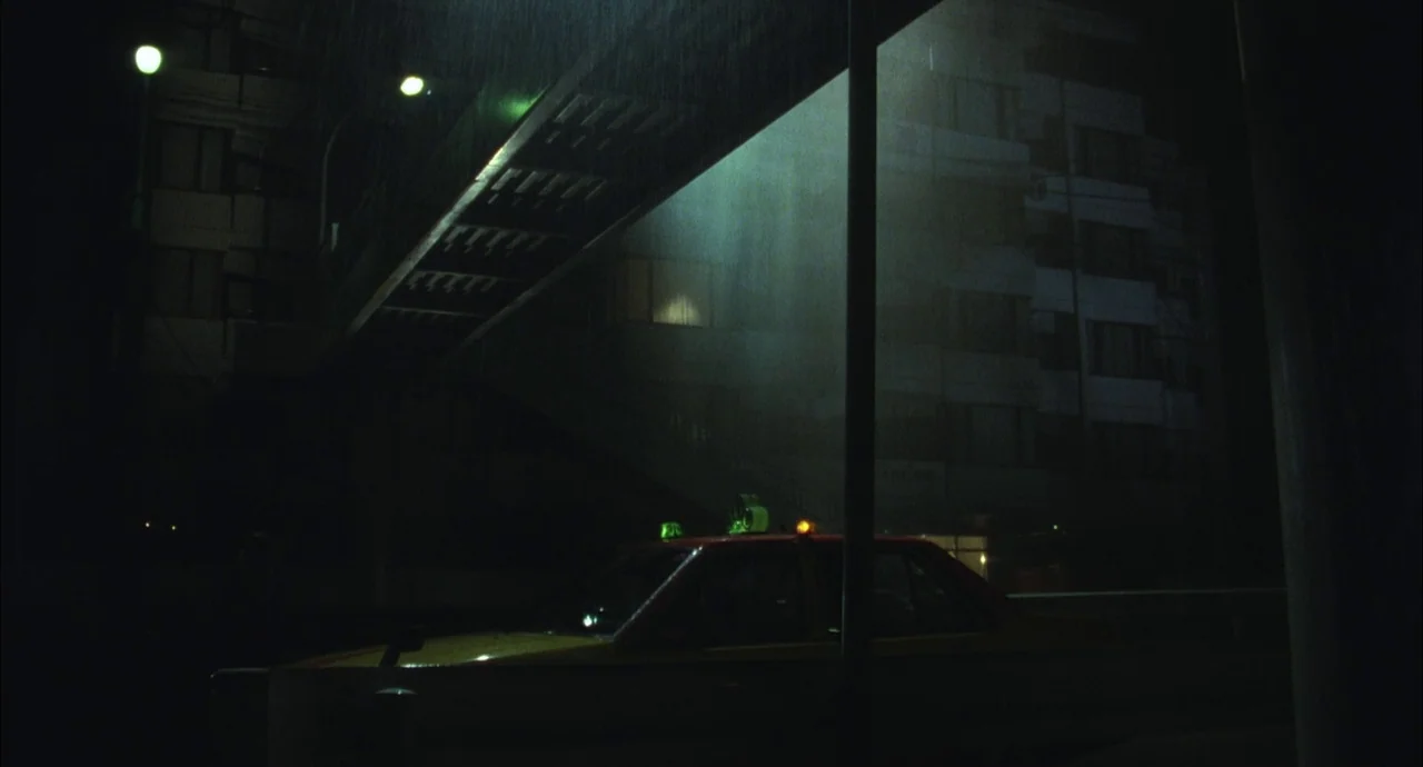 The Discarnates (1988) movie still: wide — An urban intersection at night during a rainstorm with an overpass casting shadows. A yellow taxi is…