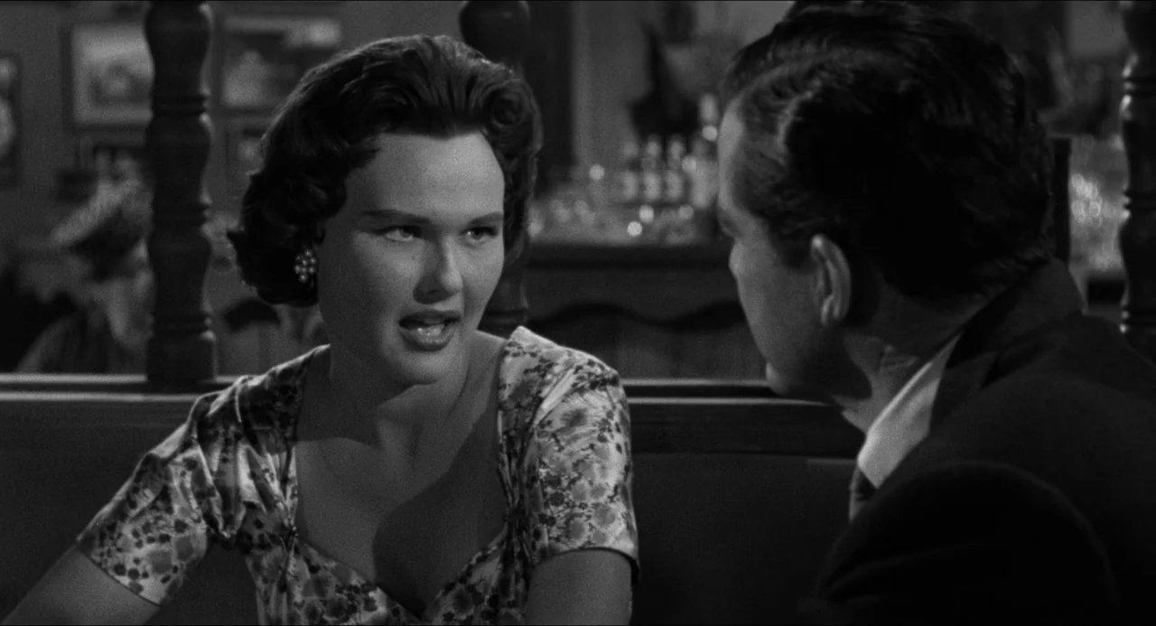 The Fearmakers (1958) movie still: medium — A dimly lit diner booth features a man and woman in conversation. The woman looks at the man while…