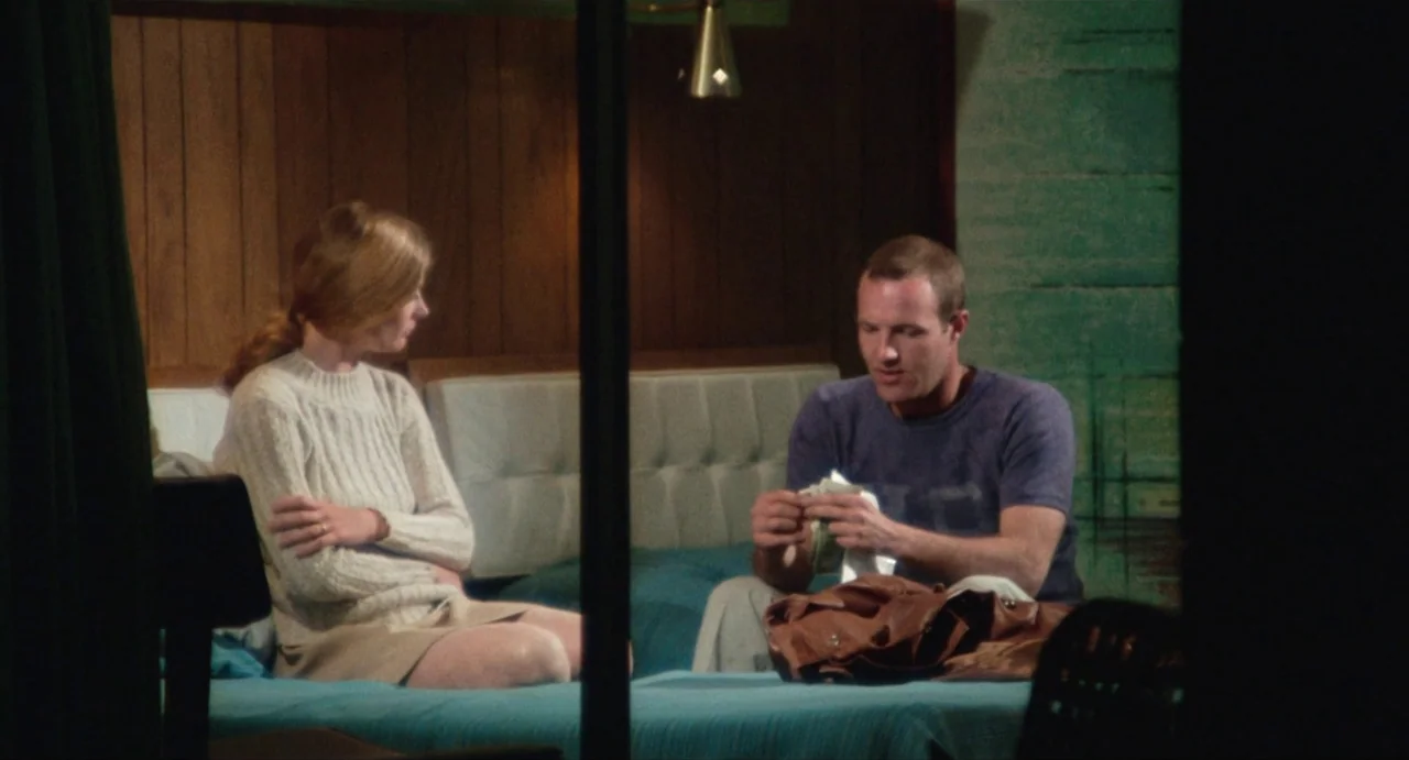 The Rain People (1969) movie still: medium — A dated motel room features wood-paneled walls and a bright teal bedspread. A man and woman sit on the…