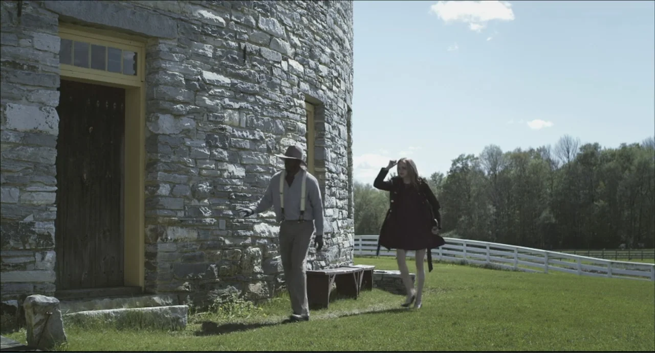 The Secret Village (2013) movie still: fullbody — A man and woman walk past the exterior of a cylindrical stone building. The structure features a…