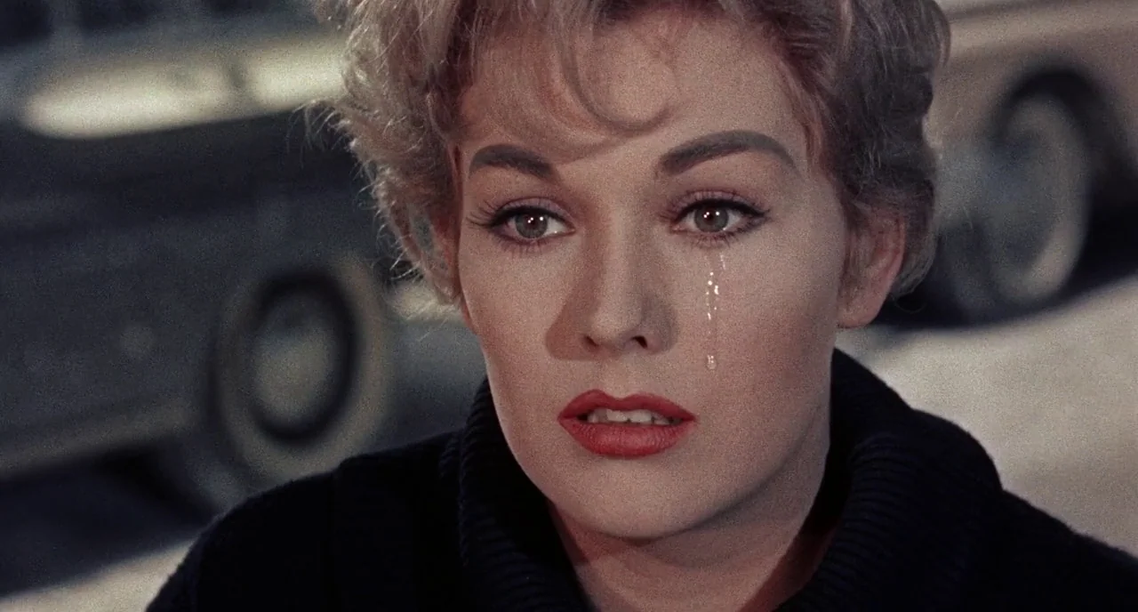 Bell Book and Candle (1958) movie still: closeup — An urban setting at night features a blurred background vehicle under dim street lighting. A…