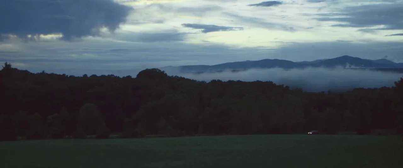 The Strange Ones (2017) movie still: establishing — A vast landscape features a dark, silhouetted forest in front of distant rolling mountains.…