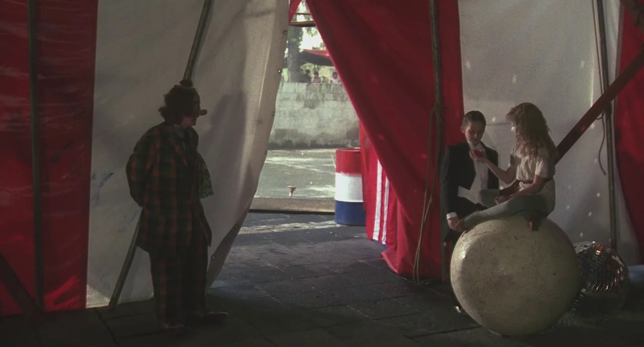 Santa Sangre (1989) movie still: wide — A circus tent interior with large red and white fabric drapes hanging down. A clown faces a young girl…