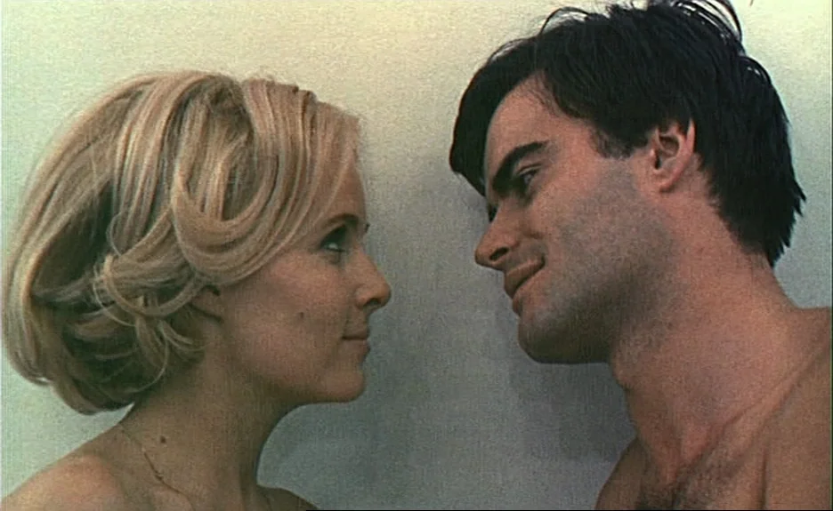 Le Bonheur (Happiness) (1965) movie still: closeup — A man and a woman stand close to each other against a plain wall. They are facing each other in…
