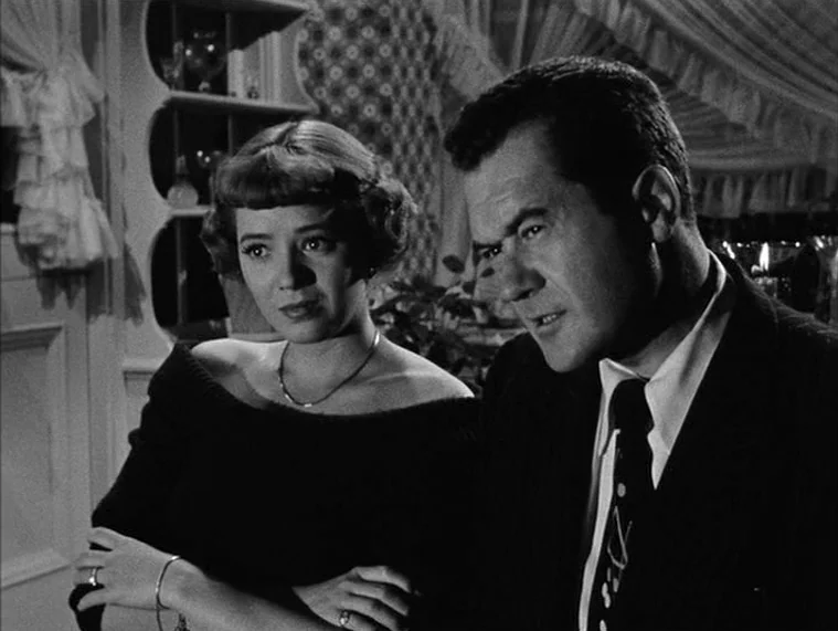 In a Lonely Place (1950) movie still: medium — A dimly lit room with ornate wallpaper and white curtains in the background. A man and a woman stand…