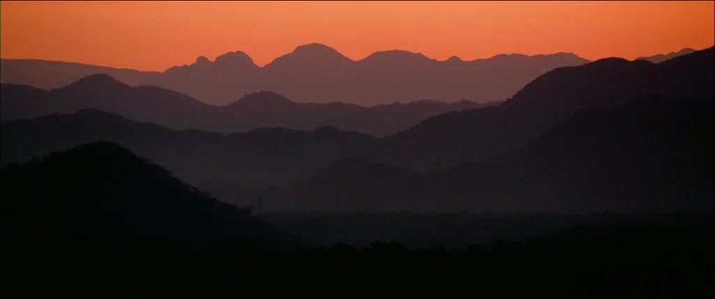 Kill Bill Vol. 2 (2004) movie still: establishing — A vast mountain range stretches across the frame in layered dark silhouettes. A glowing orange…