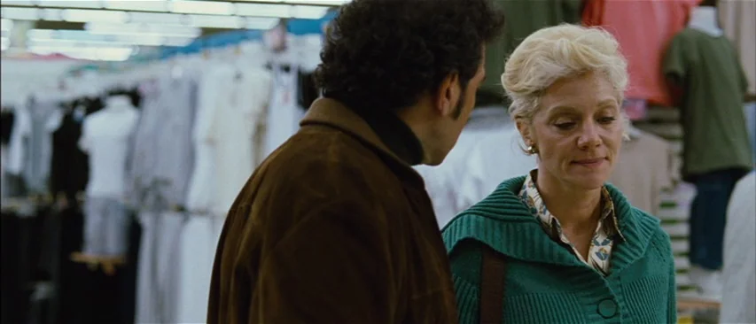 The Headless Woman (2008) movie still: medium — A retail clothing department features rows of garments on hangers in the blurred background. A man…
