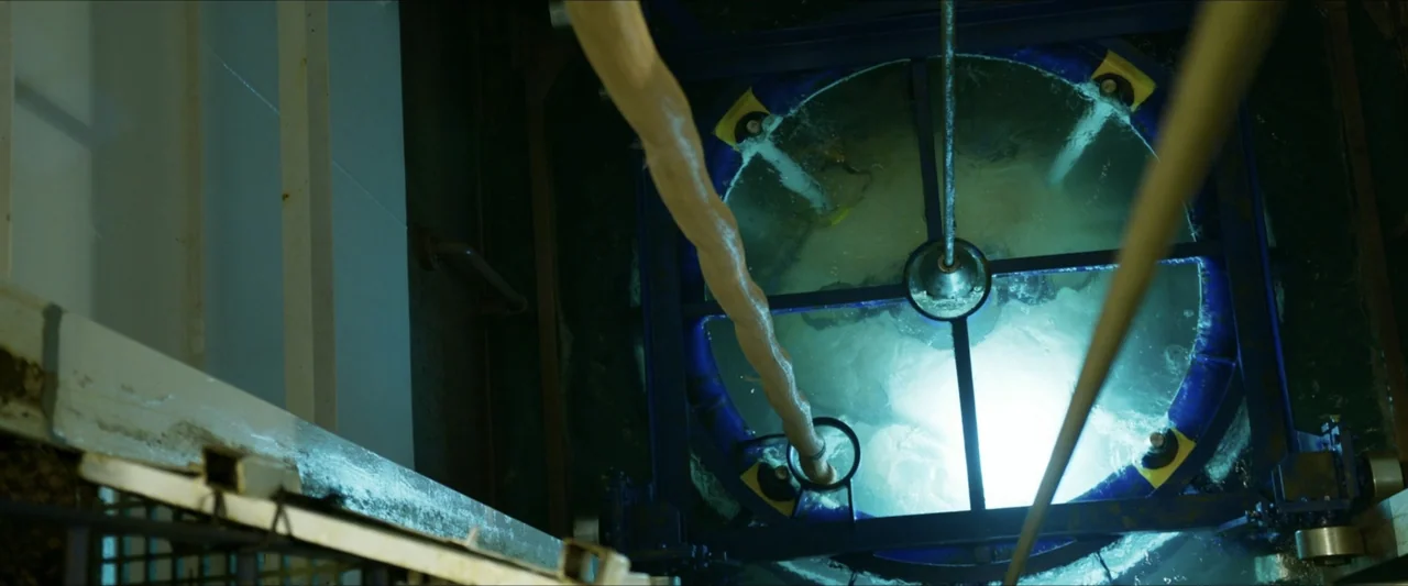 Last Breath (2025) movie still: wide — An industrial circular water tank is viewed from directly above in a dark environment. White water turbulence…